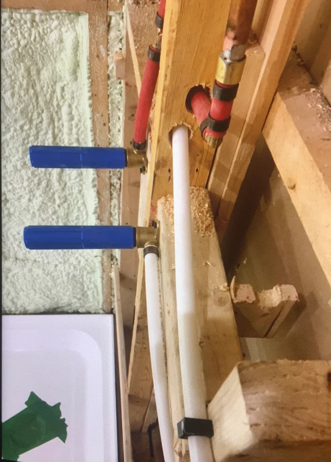 Red and white PEX supply with capped stub-outs beside a shower base, before the wall is closed.
