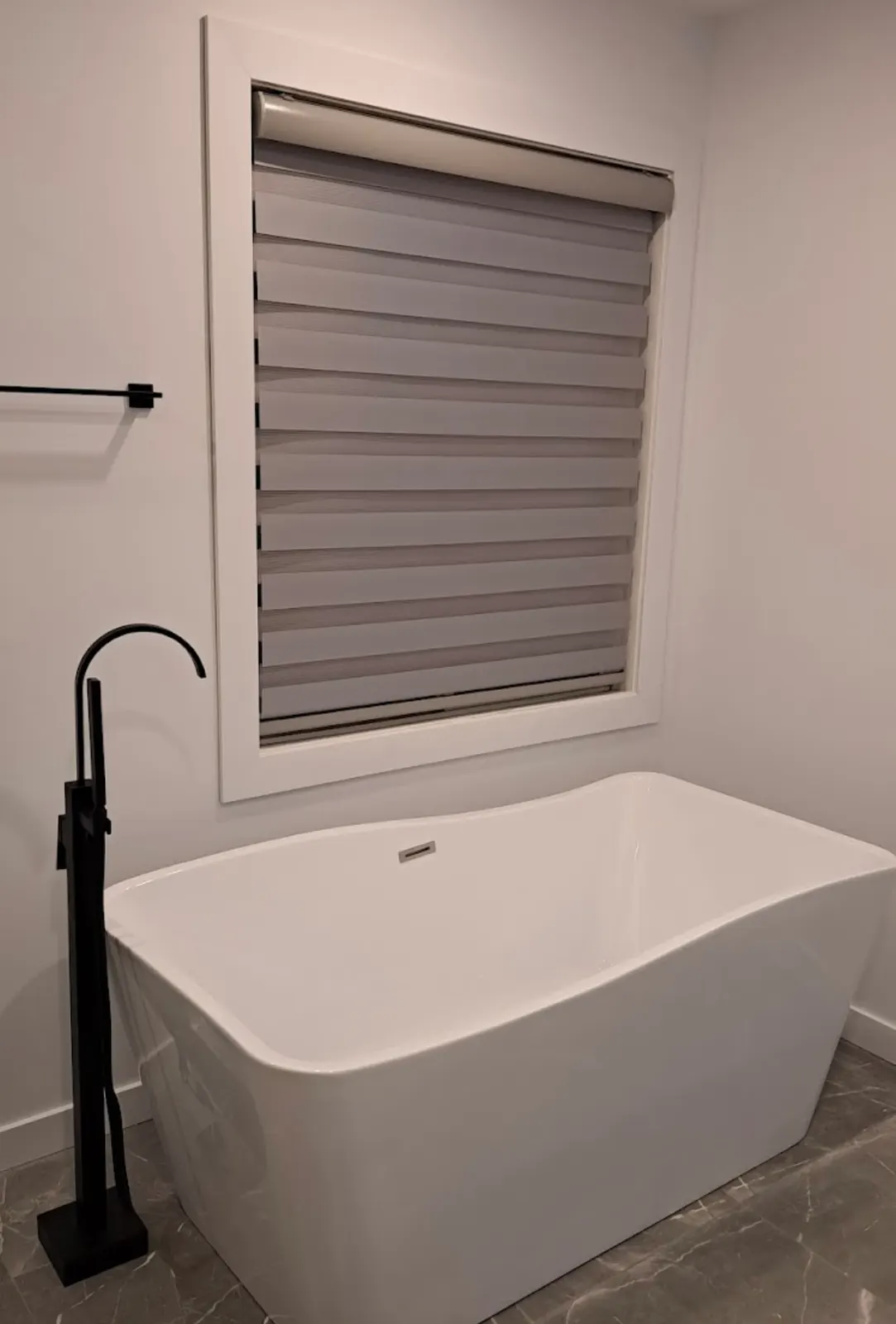 Rectangular freestanding bathtub with a black floor-mounted filler installed in front of a window.