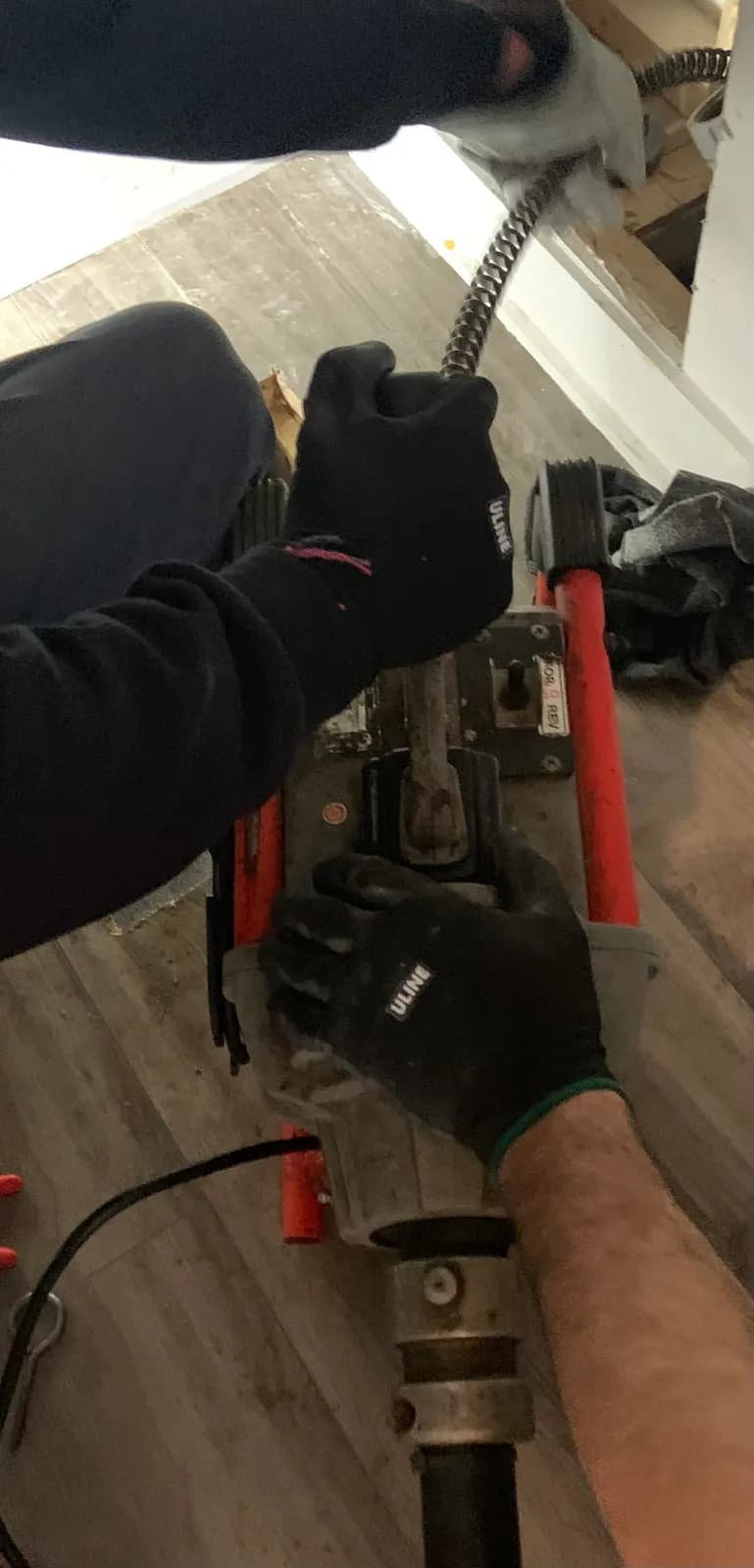 Gloved hands guiding the cable of a drain-cleaning machine into a drain line.