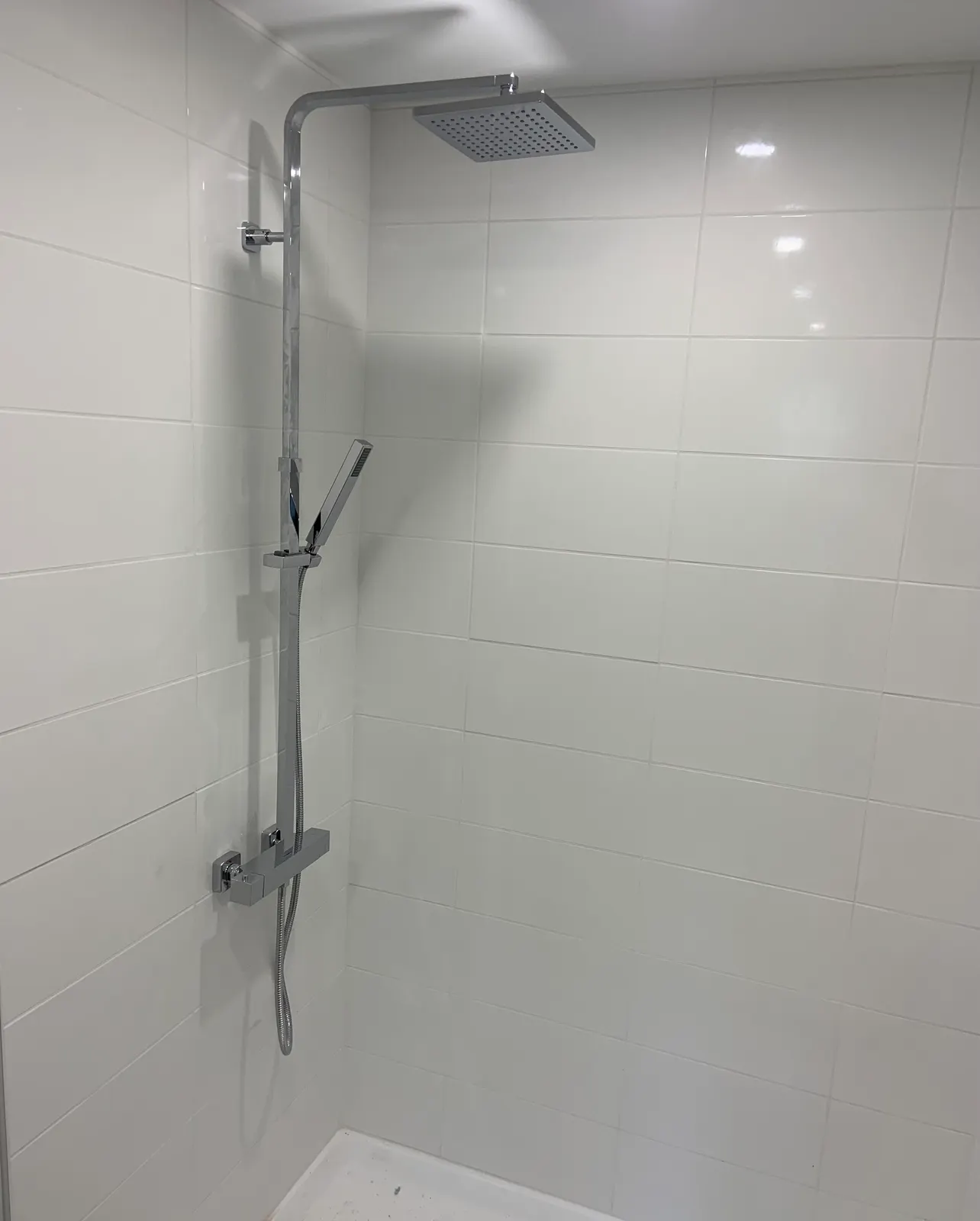 Chrome shower column with a square rain head and handshower, in a white-tiled shower.