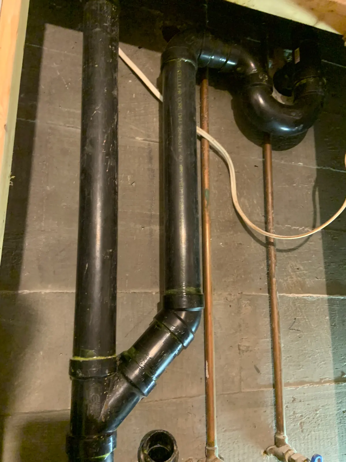 ABS drain stack and copper supply lines along a block wall in a basement.