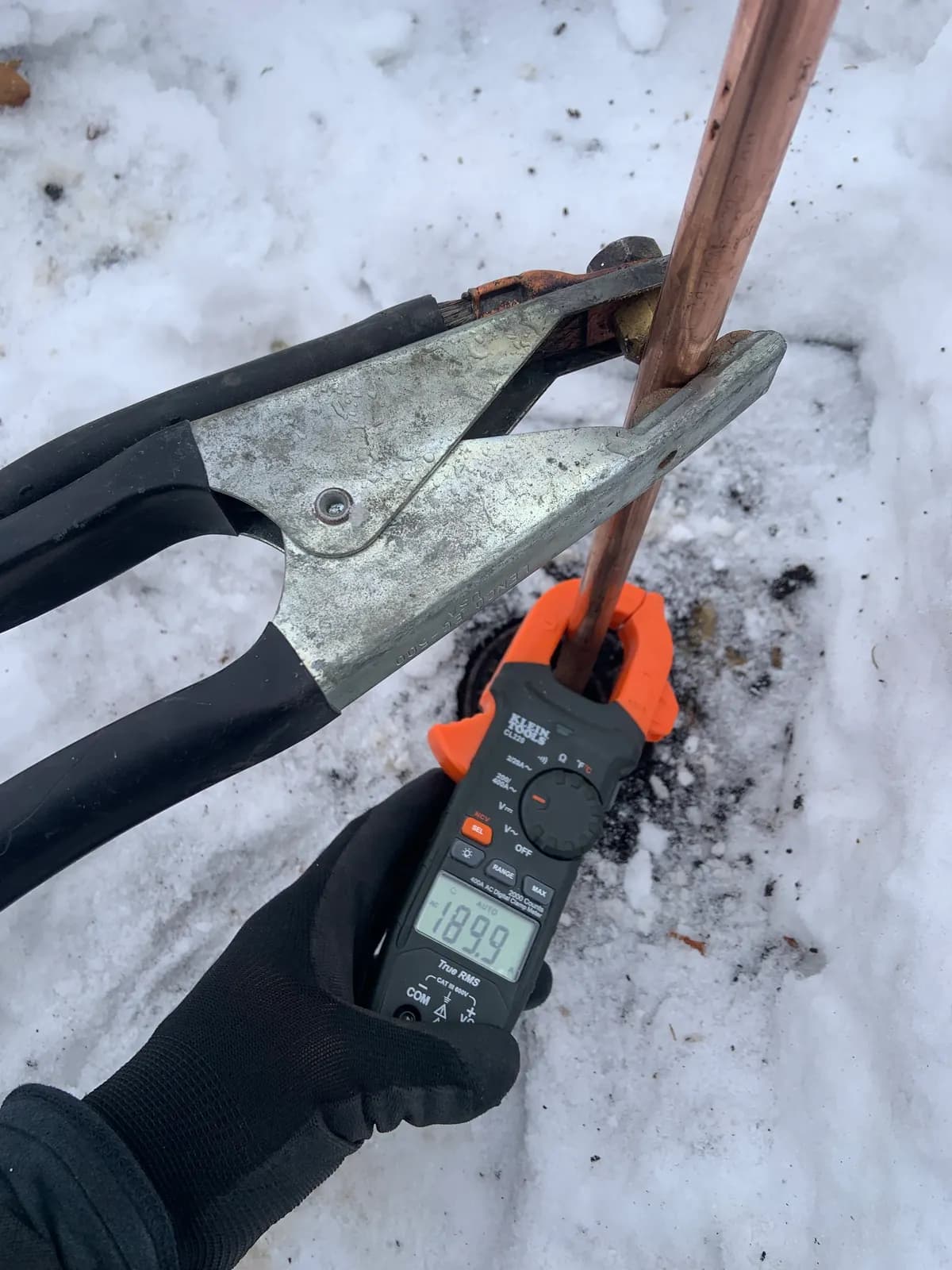 Clamp meter reading the current in a copper pipe attached to a thawing clamp, in the snow.