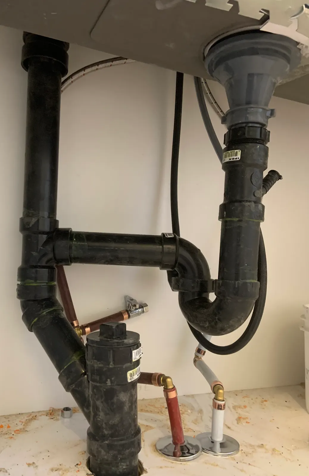 ABS trap and drain under a kitchen sink, with an air admittance valve and copper supply lines.