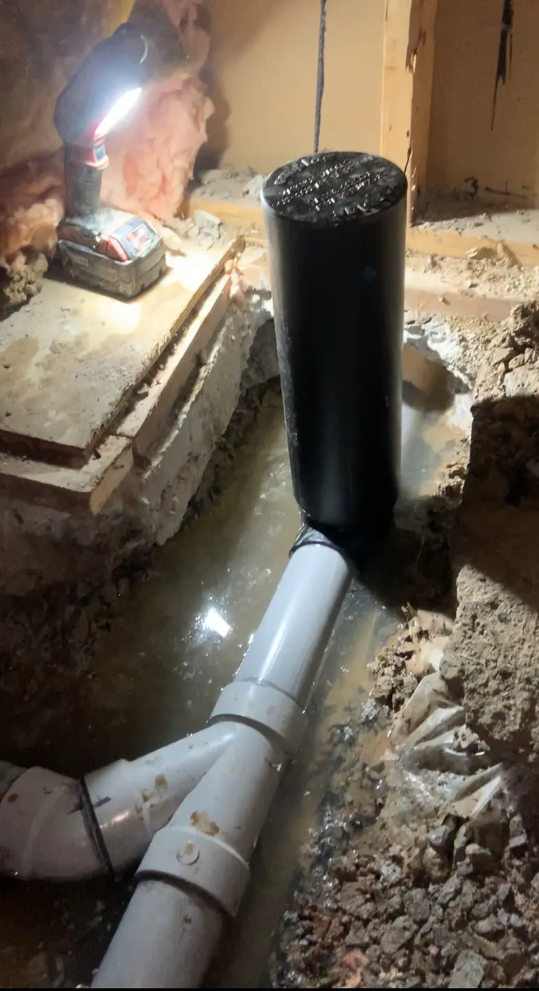 PVC drain piping and a black access riser in an excavation under the slab.