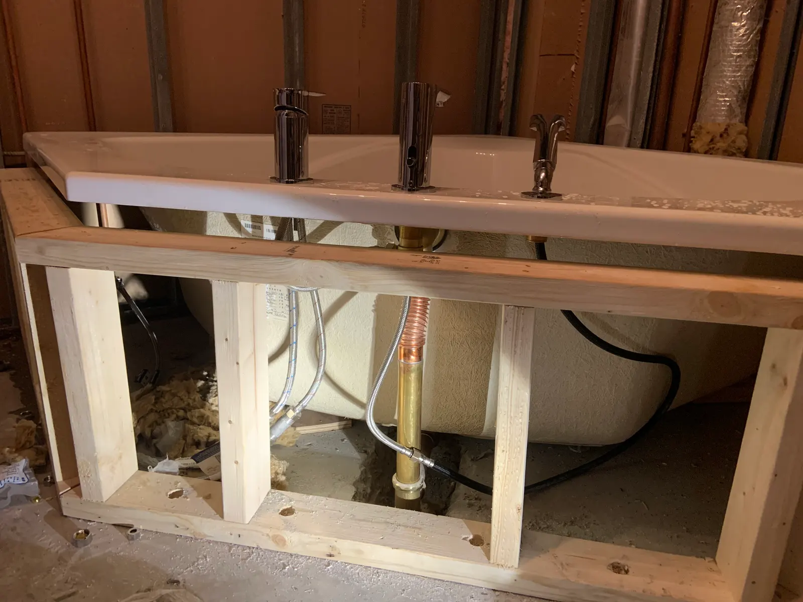 Drop-in bathtub set on its wood frame with deck-mounted fixtures installed, before the apron is finished.