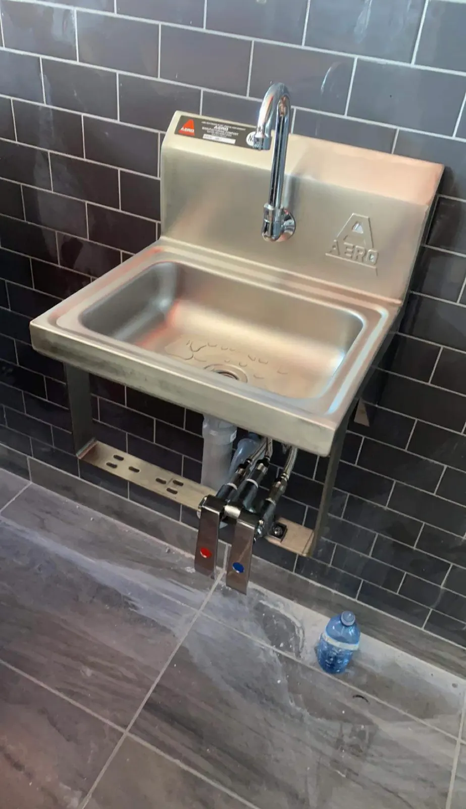 Stainless-steel commercial hand sink with hands-free controls, installed against dark tile.