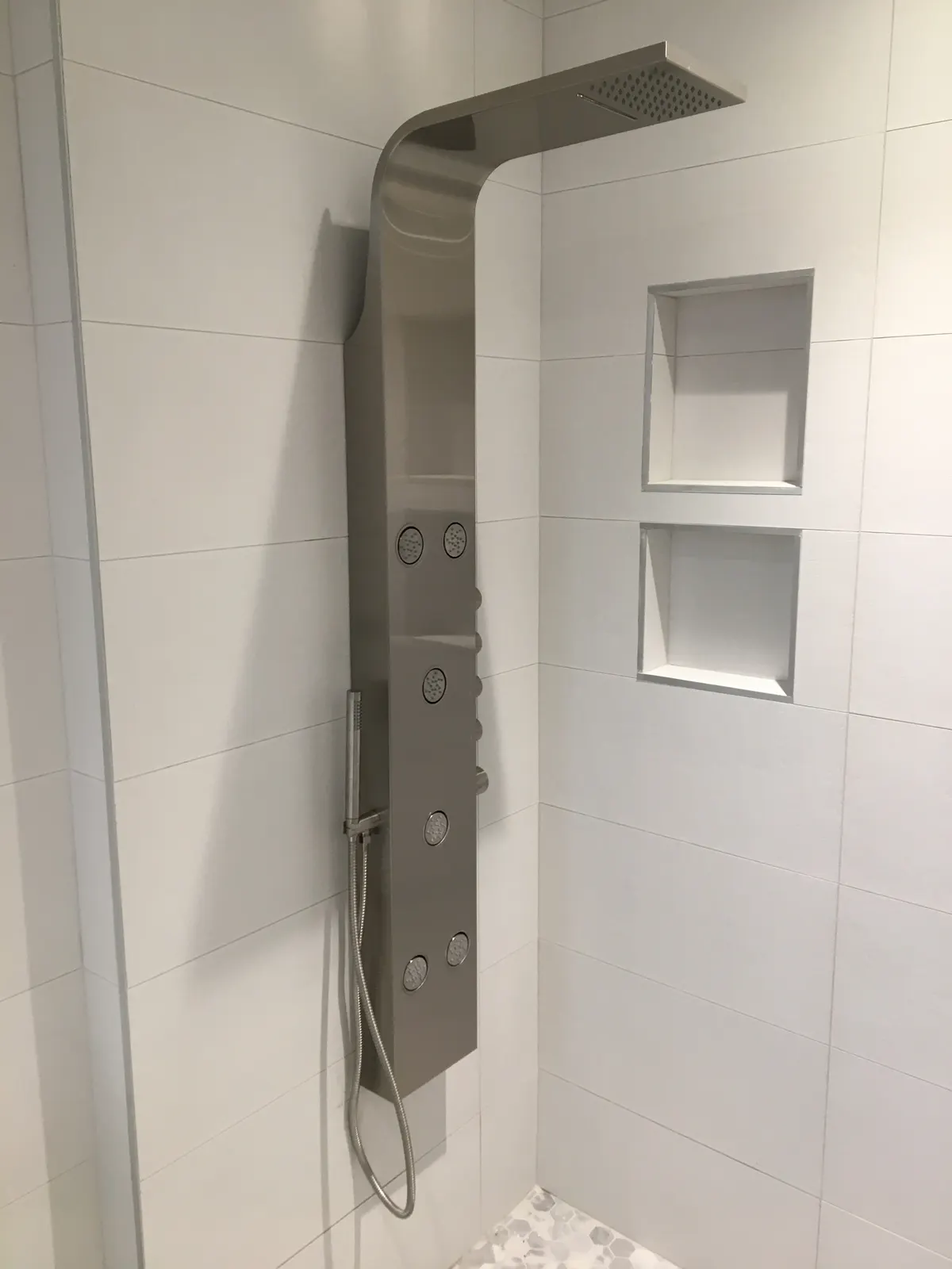 Stainless-steel shower panel with a rain head, massage jets and handshower, beside two wall niches.