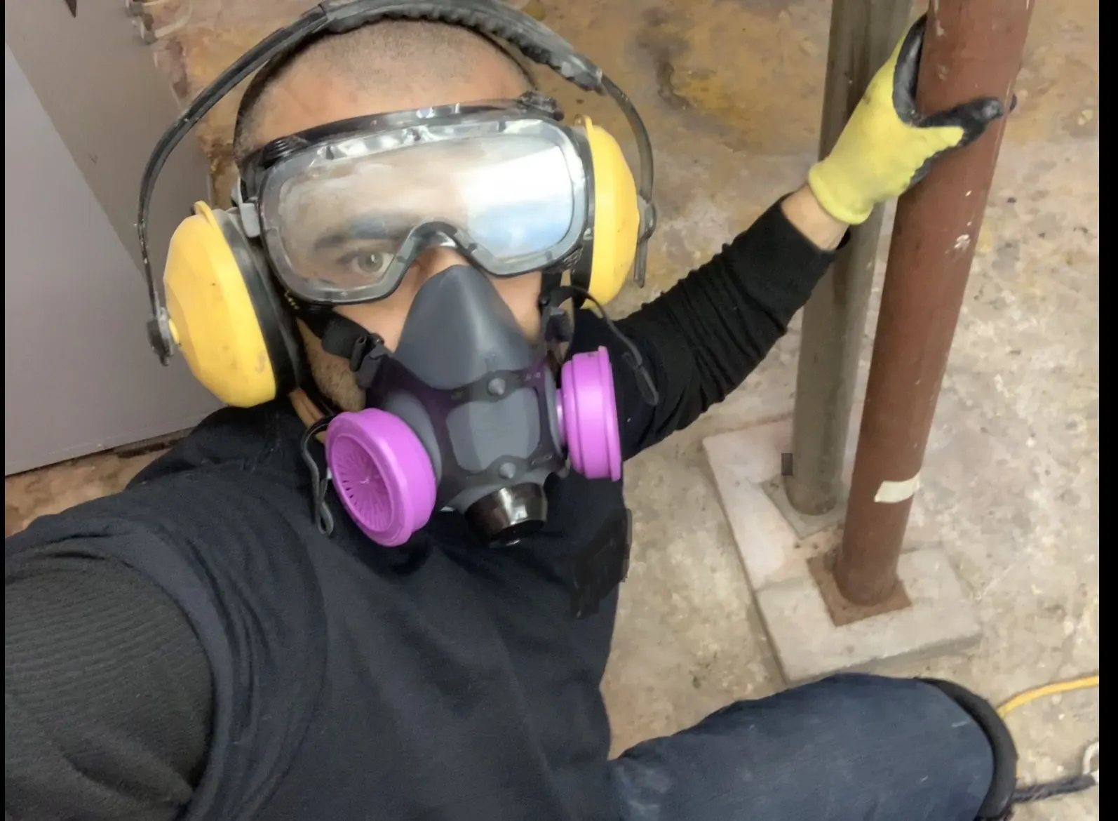 Plumber wearing a half-face respirator, sealed goggles and ear protection on a job site.