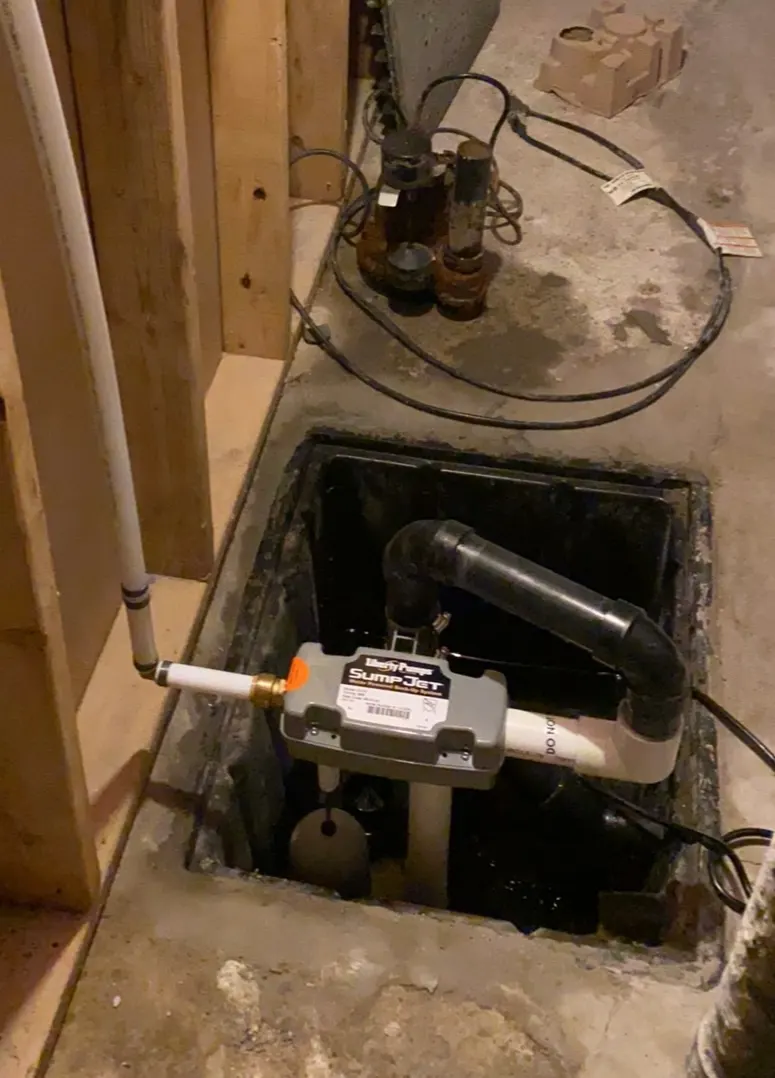 Open sump pit showing an installed pump and a backup pump connected to the discharge piping.