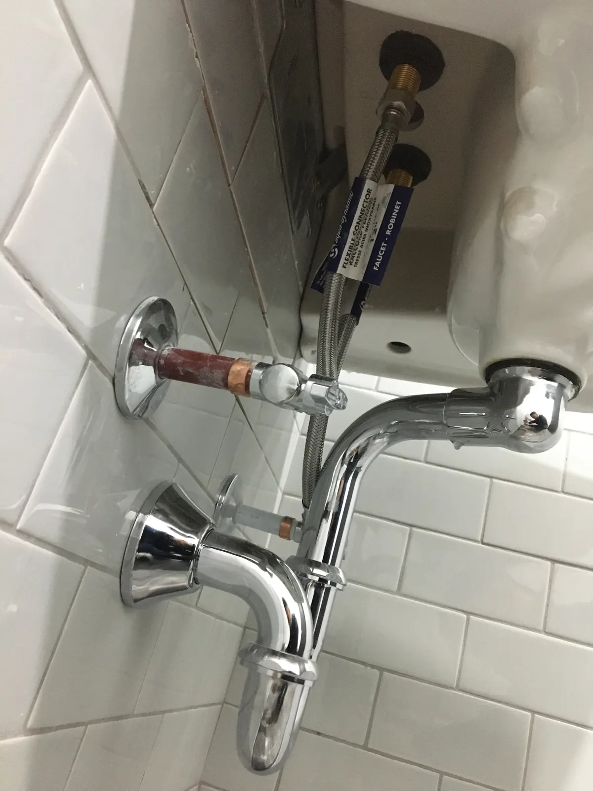 Raccords d’alimentation en tresse d’acier inoxydable, valves d’arrêt et siphon chromé sous un appareil sanitaire.