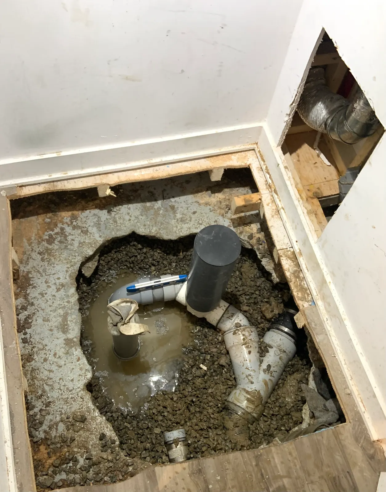 Opened concrete slab with new PVC drain piping laid level in the gravel.