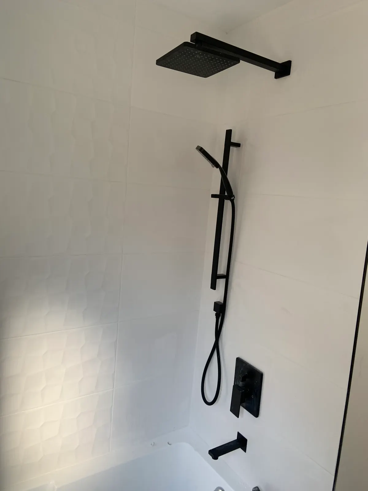 Matte-black shower fixtures: rain head, slide-bar handshower, recessed valve trim and tub spout.
