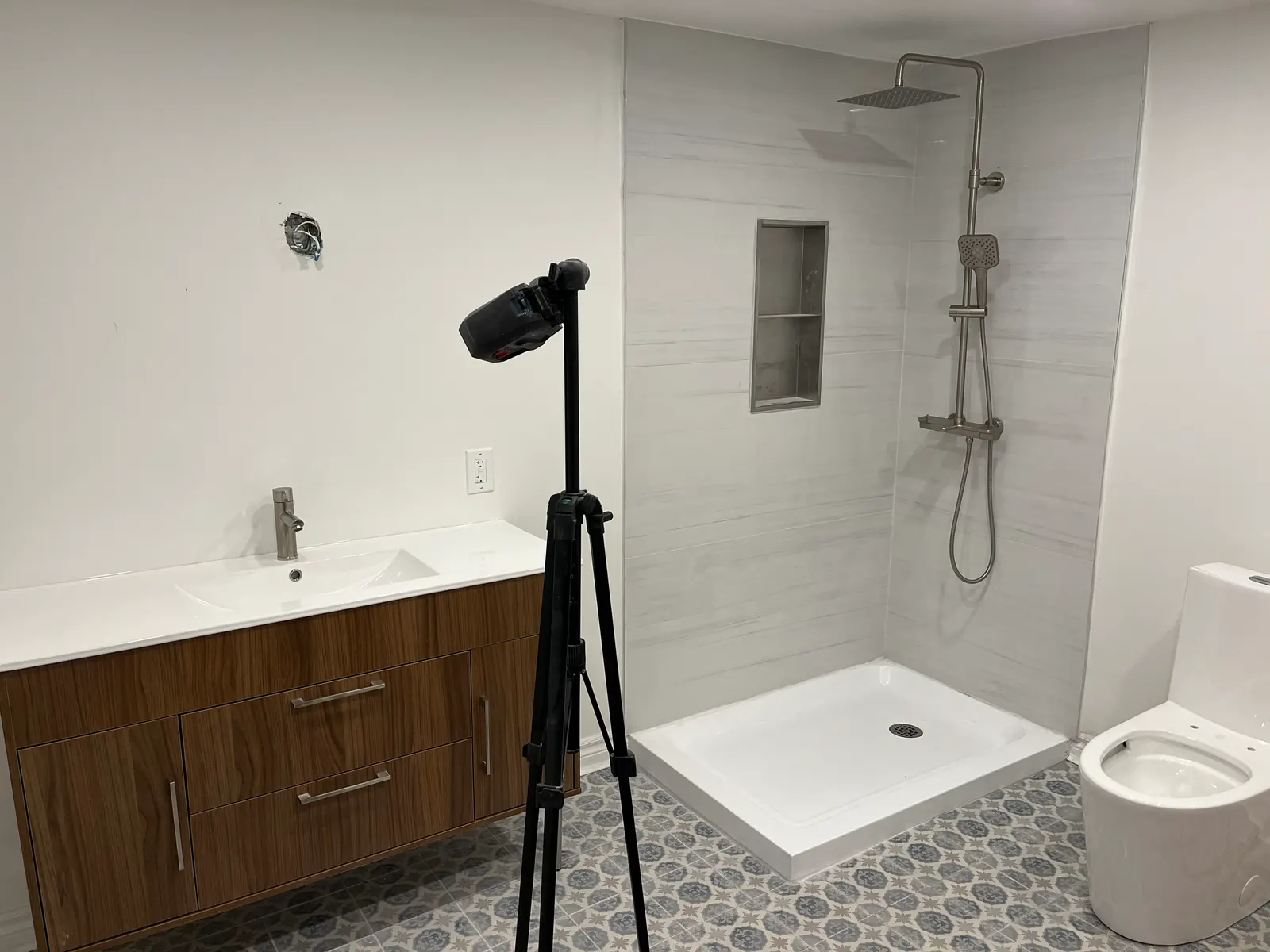 Finished bathroom with an acrylic shower base, shower column, wood vanity and one-piece toilet.