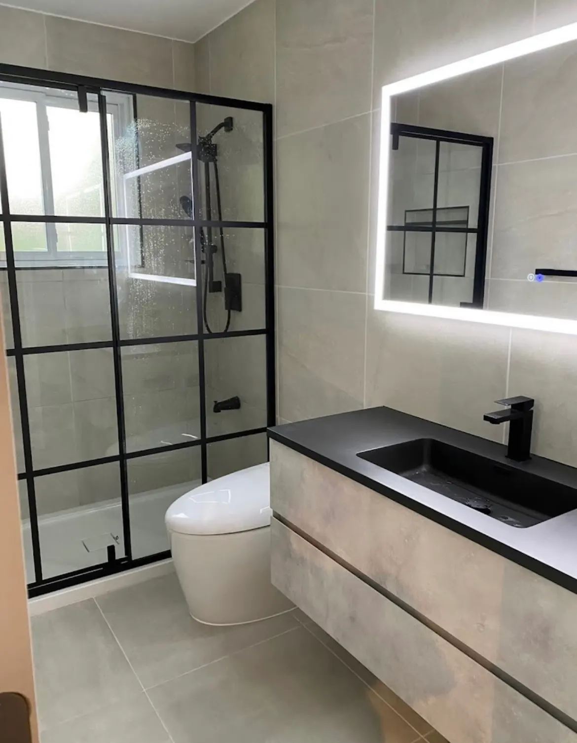 Bathroom with a black grid-style glass shower door, backlit mirror, floating vanity and black basin.