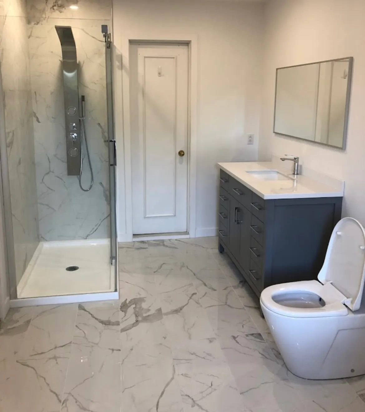 Bathroom with a glass shower enclosure, built-in shower column, grey vanity and elongated toilet.