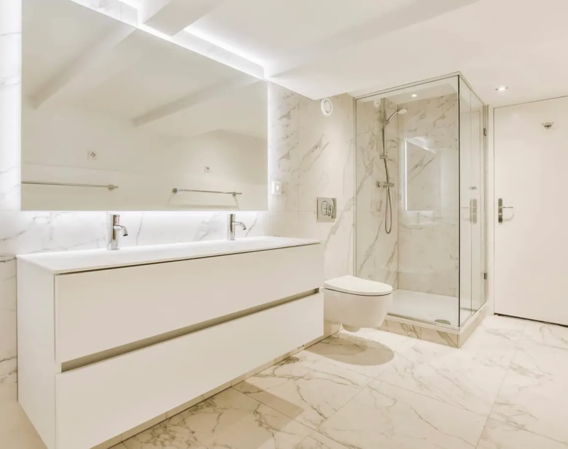 Salle de bain contemporaine avec toilette suspendue, douche d’angle vitrée et vanité double à deux robinets.