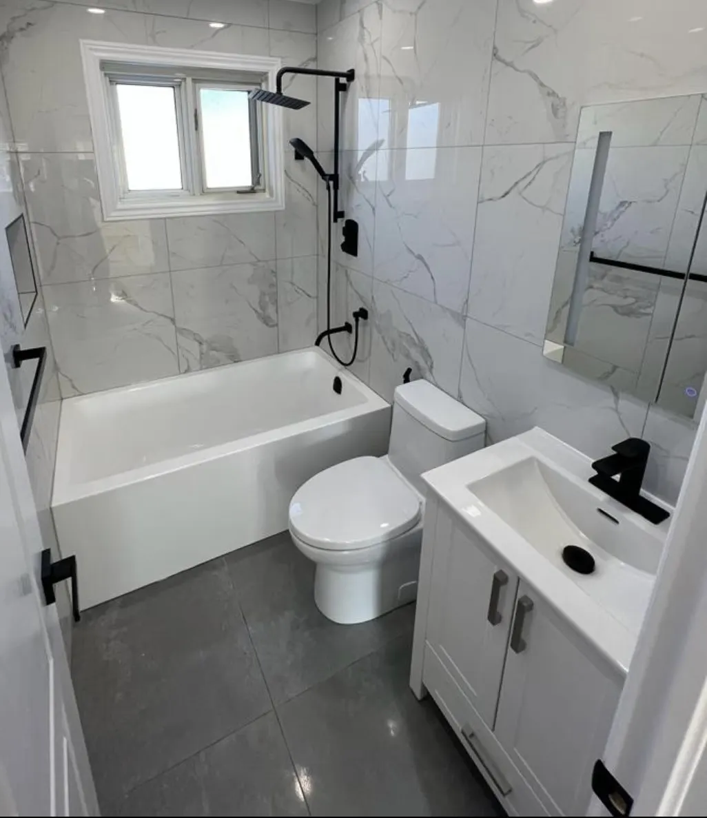 Salle de bain rénovée avec baignoire encastrée, toilette, vanité et robinetterie noire sur céramique effet marbre.