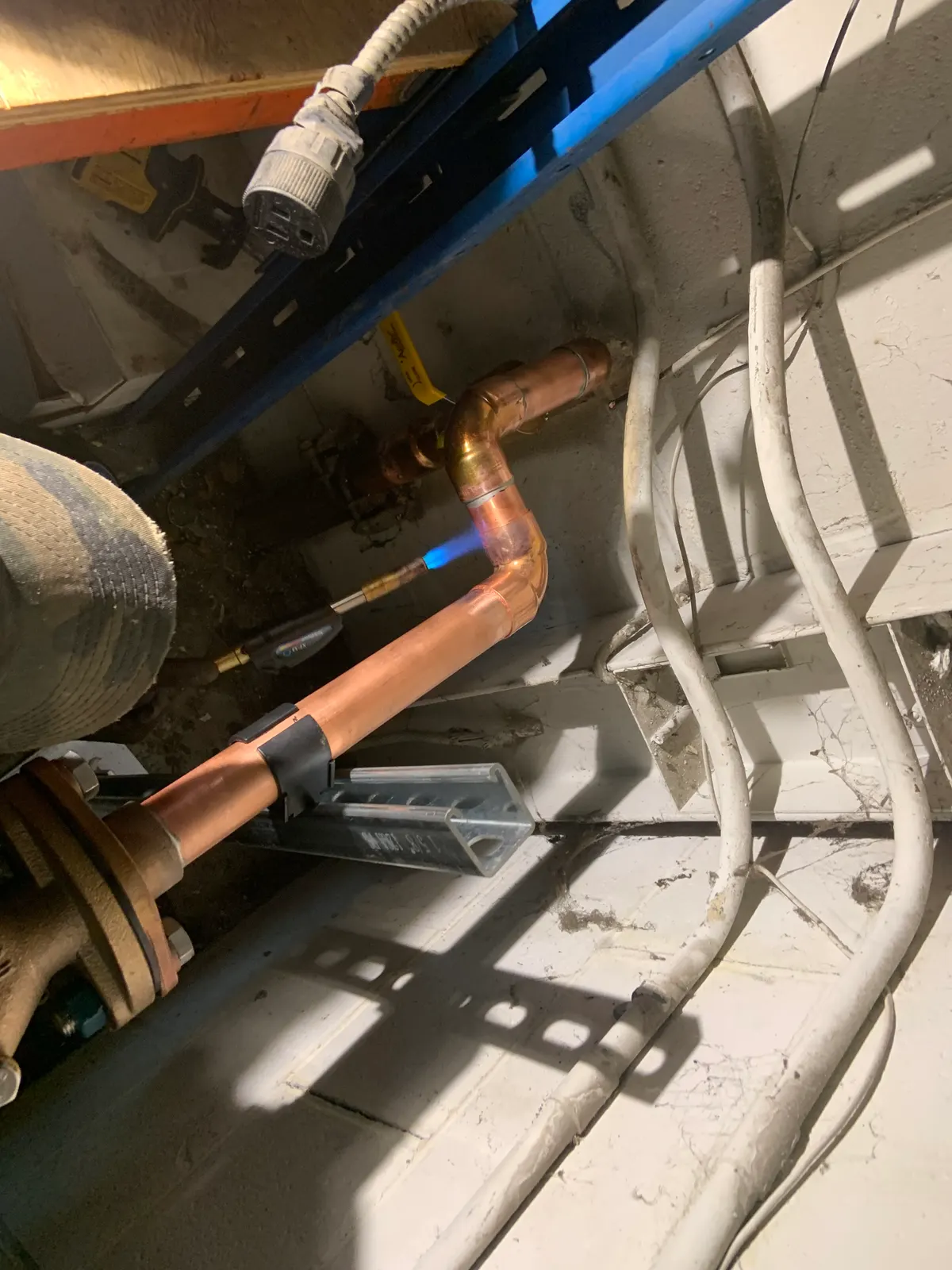 Torch-soldering an elbow on a copper pipe secured to a support channel.