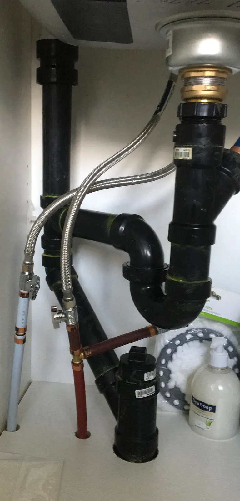 Air admittance valve on the ABS drain of a kitchen sink, with braided-steel supply lines.