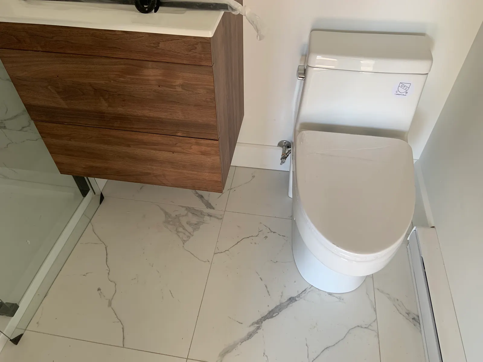 One-piece toilet and floating wood vanity on a marble-effect tile floor.
