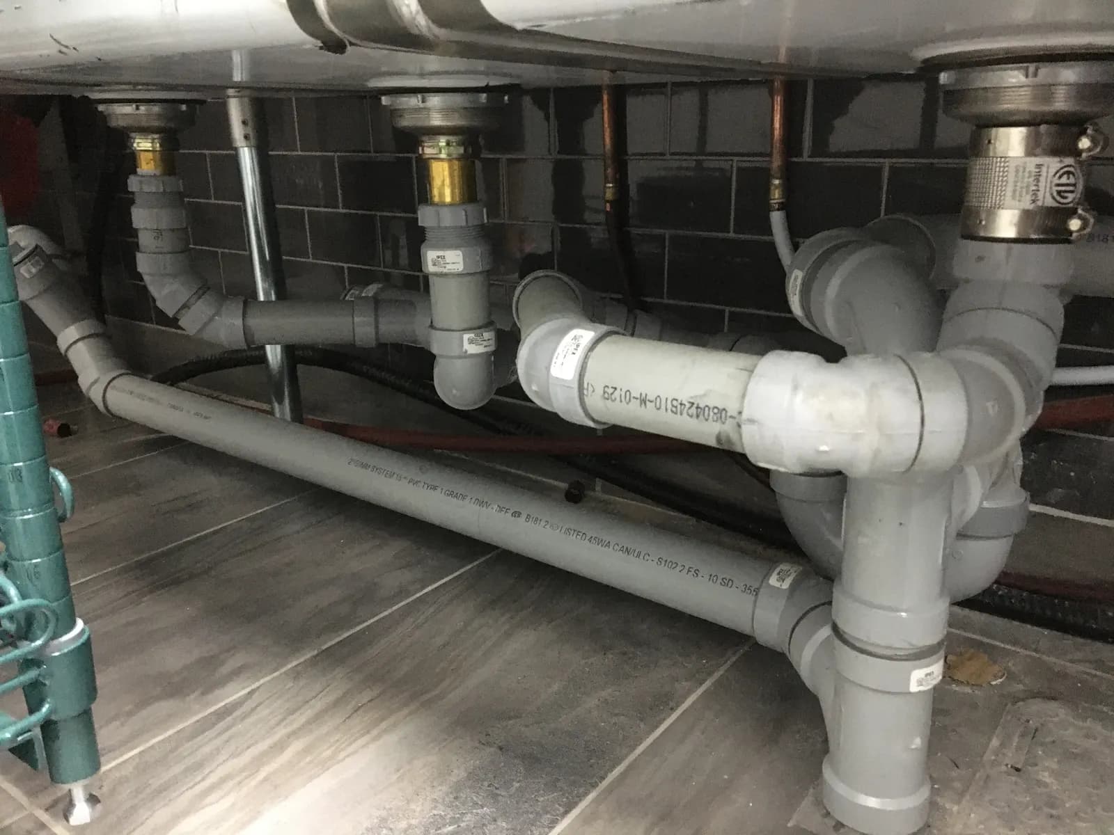 Grey drain piping connected under a multi-compartment stainless-steel commercial sink.
