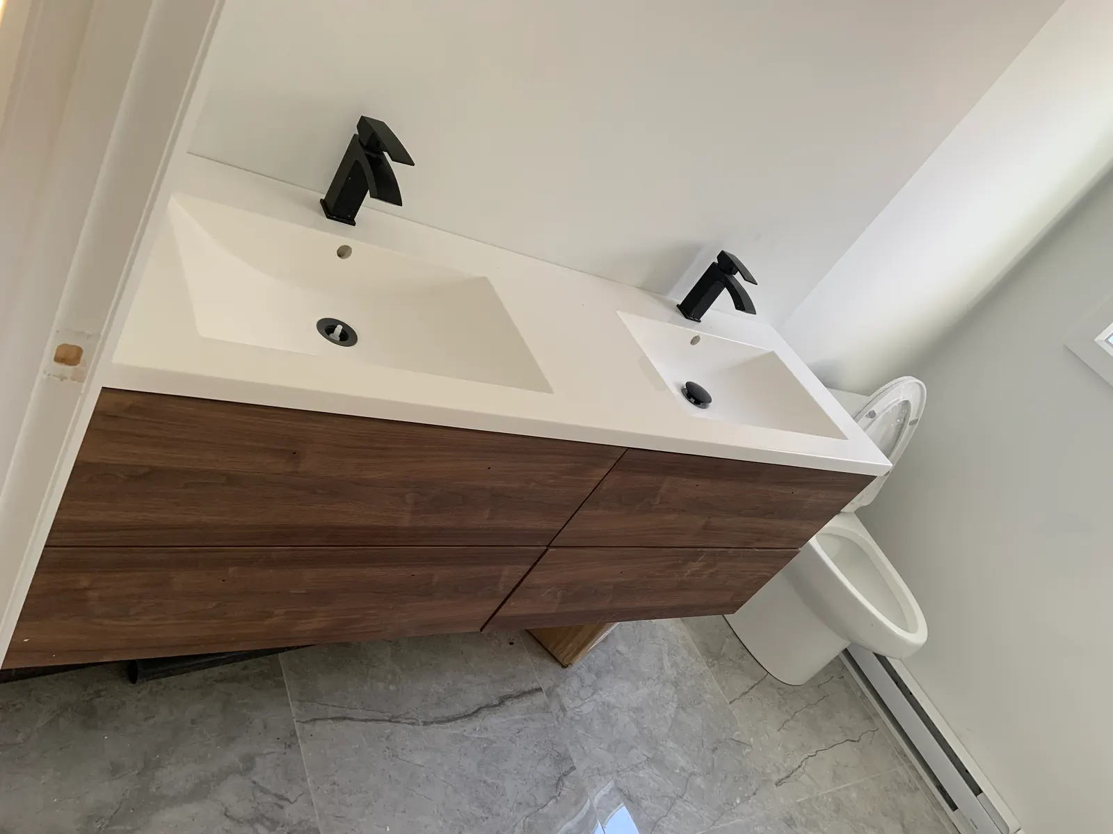 Double wood vanity with two basins and matte-black faucets, next to a new toilet.